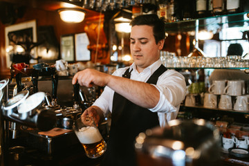 A young caucasian waiter pours beer at a bar