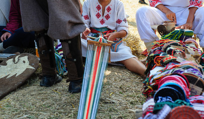 Fototapeta na wymiar Woman dressed in colorful traditional native Serbian closing knitting a carpet with national pattern