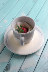 Red ripe strawberries fall into a Cup of milk. A Cup of milk on a turquoise wooden table. Splashes of milk.