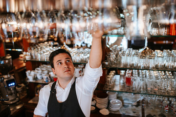 
A young caucasian waiter picks up glasses at a bar