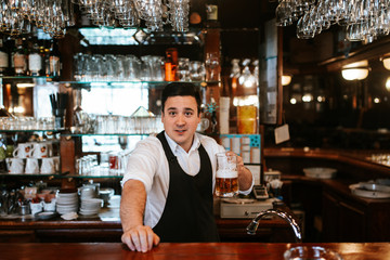 A young caucasian  waiter drinks beer at a bar