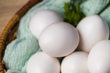 White eggs in a wicker basket with a mint cloth. eggs on a light wooden background