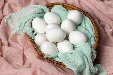 White eggs in a wicker basket with a mint cloth. eggs on a pink background