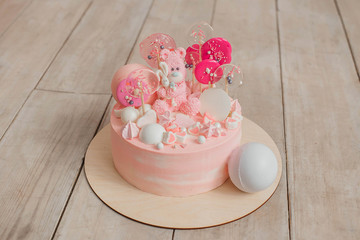 light pink cake on a white wooden floor with bears and sweets on top, one year celebration