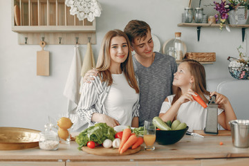 Family in a kitchen. Blonde in a white t-shirt. Woman with vegetables