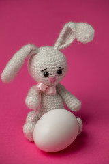 Easter knitted rabbit with a painted egg on a pink background. Concept of the Easter holiday