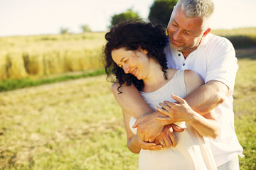 Aduld couple in a summer field. Handsome senior in a white shirt. Woman in a white dress