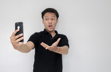 Angry Asian young man get mad on the smartphone. Indonesia Man wear black shirt Isolated grey background.
