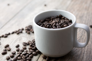 A view of a white mug with dark roasted coffee beans in a restaurant or kitchen setting.