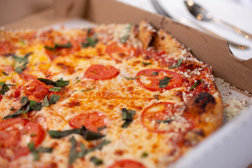 A closeup view of a Margherita pizza pie inside a pizza box, in a restaurant or kitchen setting.