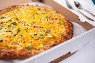 A closeup view breakfast pizza pie, inside a pizza box, in a restaurant or kitchen setting.