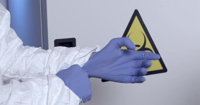 Lab technician puts on and adjusts blue latex gloves on the background of the bio hazard sign. Compliance with safety in the laboratory.
