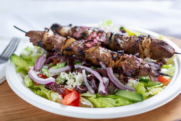 A view of a plate of beef shish kabob on a salad, in a restaurant or kitchen setting.