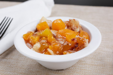 A closeup view of a bowl of peach cobbler, in a restaurant or kitchen setting.