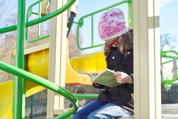 Smart child girl, 8-9 years old, in jacket hat glasses, reading book