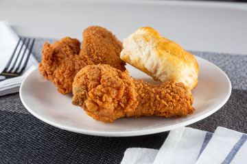 A view of a plate of fried chicken and a side biscuit, in a restaurant or kitchen setting.