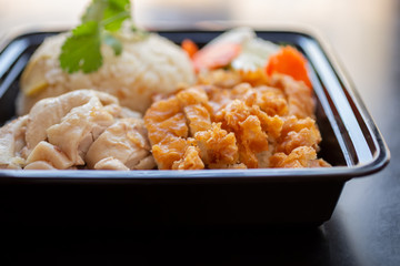 A closeup view of a Hainanese and crispy chicken combination entree, in a restaurant or kitchen setting.