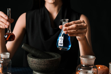 Female alchemist making potion on dark background