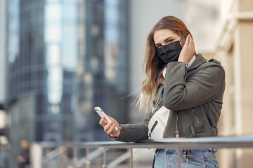 Fototapeta premium Woman in the city. Person in a mask. Coronavirus theme. Girl walks with phone and headphones.
