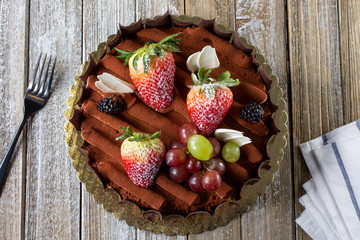 A top down view of a chocolate cake with fruit toppings, in a restaurant or kitchen setting.