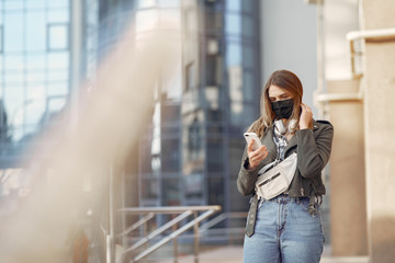 Fototapeta premium Woman in the city. Person in a mask. Coronavirus theme. Girl walks with phone and headphones.