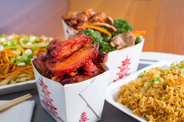 A view of an array of Chinese take out, featuring BBQ pork, beef broccoli, fried rice and chow mein.
