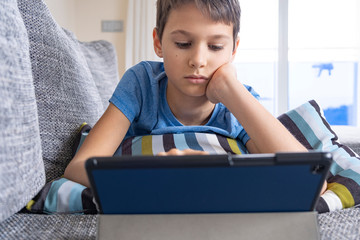 Boy lying on sofa with digital tablet computer at home. Technology, ditance education, online learning, playing games concept