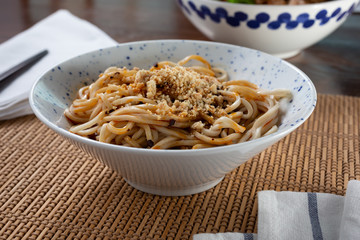 A view of a bowl of dan dan noodles, in a restaurant or kitchen setting.