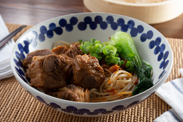A view of a bowl of pork ribs and dan dan noodles, in a restaurant or kitchen setting.