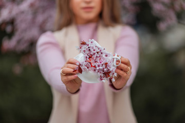 Pretty woman is wearing protection face mask decorated with pink flowers, virus and spring concept.