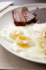 A closeup view of a Latin American breakfast plate in a restaurant or kitchen setting, featuring sunny side up eggs and fried plantains. 
