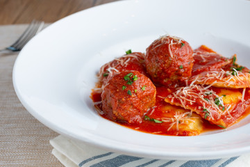 A closeup view of a plate of ravioli and meatballs in a restaurant or kitchen setting.