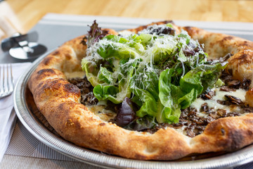 A view of a rustic pizza in a restaurant or kitchen setting, featuring toppings as mushrooms and gem lettuce greens.
