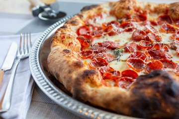 A closeup view of a rustic pizza pie in a restaurant or kitchen setting, featuring toppings as pepperoni.
