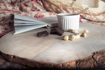 An open book, cashews, chocolate and pudding in a ceramic cup are on a wooden tray.