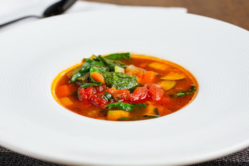 A closeup view of a bowl of minestrone soup, in a restaurant or kitchen setting.