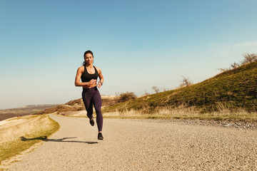 Motivated female athlete road running while exercising outdoors.