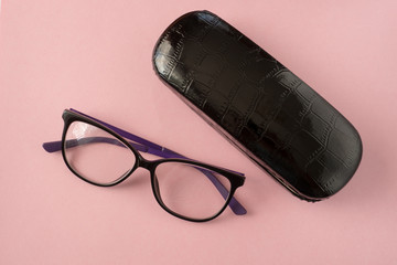 Glasses and black case for glasses close-up on a pink background.