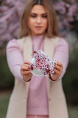 Pretty woman is wearing protection face mask decorated with pink flowers, virus and spring concept.