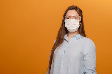close-up portrait of young woman on yellow orange background in protective medical mask, coronavirus pandemic