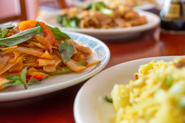 A view of several dinner plates on a table in an Asian restaurant setting, featuring a plate of Thai drunken noodles.
