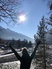 a girl in the mountains stretches her hands up to the sun