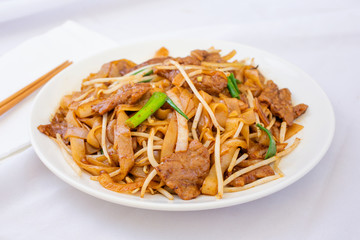 A view of a Chinese plate of beef chow fun, in a restaurant or kitchen setting.