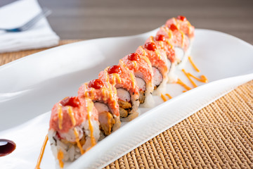 A view of a colorful sushi roll with tempura shrimp and imitation crab, in a restaurant or kitchen setting.