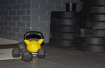 one yellow kettlebell and two black dumbbells on a gray mat