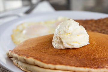 A closeup view of a stack of pancakes with a dollop of whipped butter on top, in a restaurant or kitchen setting.