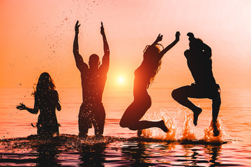 Happy friends jumping inside water on tropical beach at sunset - Group of young people having fun...