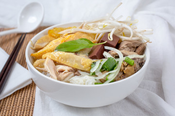 A view of a bowl of pho with chicken thigh, liver, and blood, in a restaurant or kitchen setting.