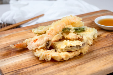 A view of a wooden board with several pieces of tempura vegetables and shrimp, in a restaurant or kitchen setting.