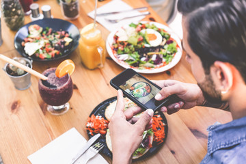 Hands view of influencer man eating brunch while making video of dish with mobile phone in trendy bar restaurant - Healthy lifestyle, technology and food trends concept - Focus on man hand